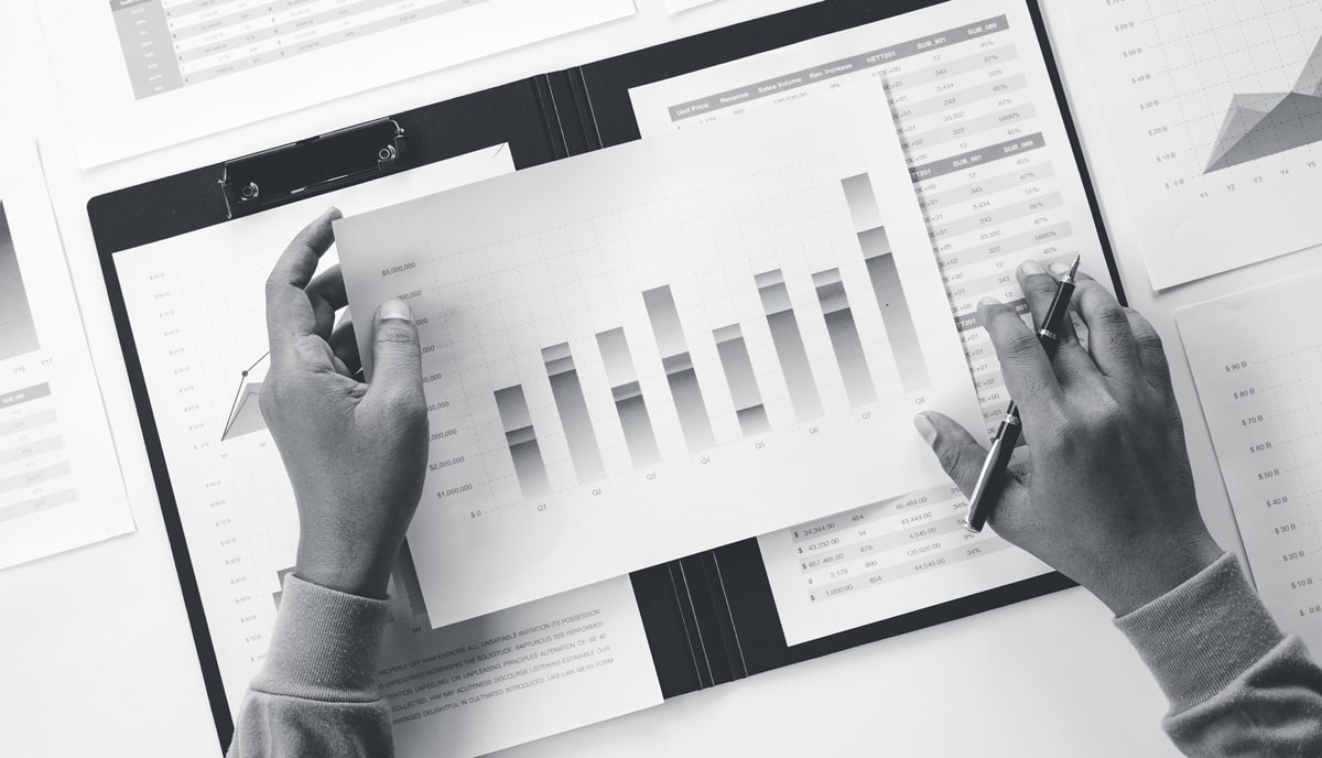 Hands holding a paper chart with pen and multiple other paper reports nearby