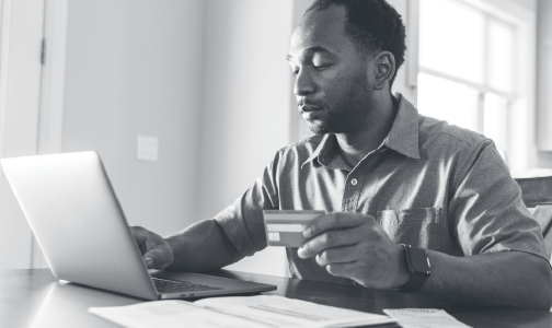 Man sitting at a table with his credit card in hand and laptop nearby