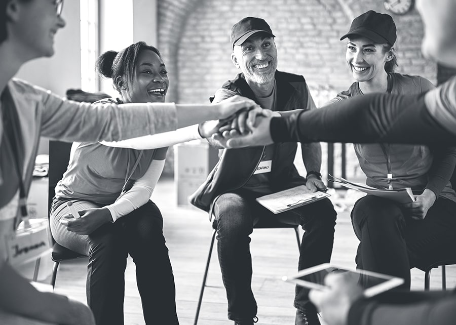 Group of people placing their hands together in the middle of a circle to express teamwork