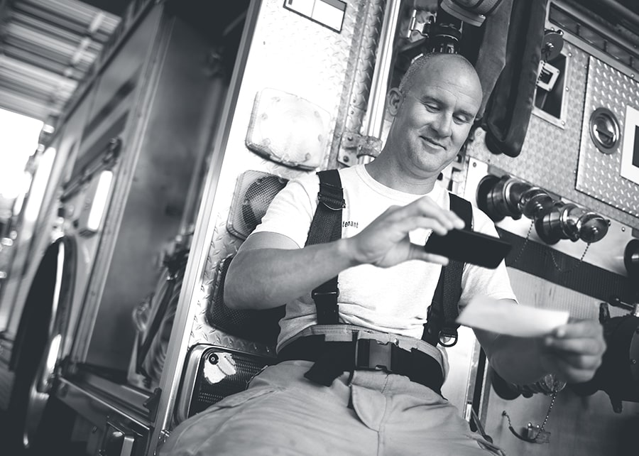 Firefighter on break seated on the firetruck while making a mobile deposit on his cell phone
