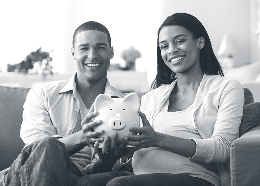 Smiling man and woman sitting on a couch holding a piggy bank together