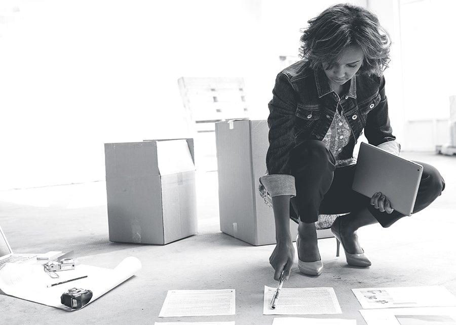 Woman looking over paperwork organized on the floor with moving boxes behind her