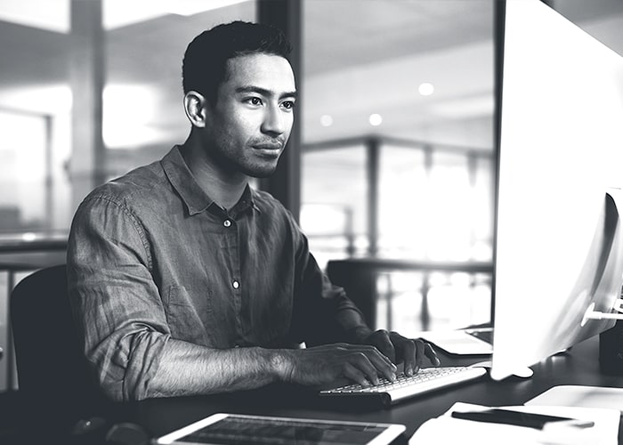 Man sitting at desk staring at computer screen with hands on computer keyboard