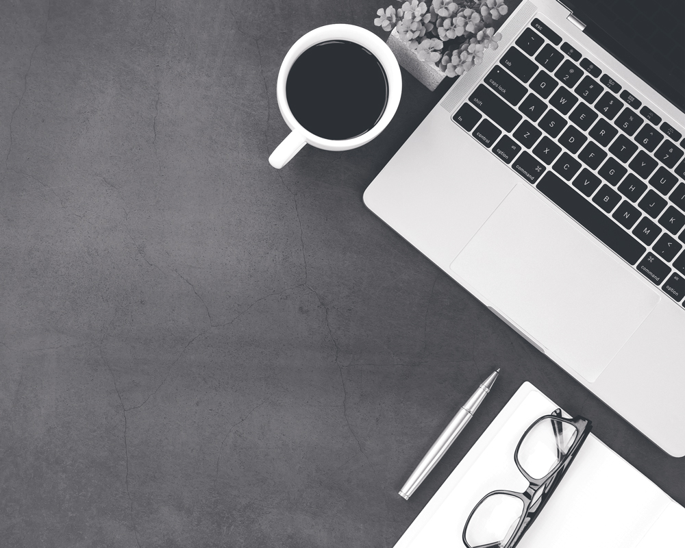 Laptop, cup of coffee, flowers, paperwork, reading glasses, and pen on a desk