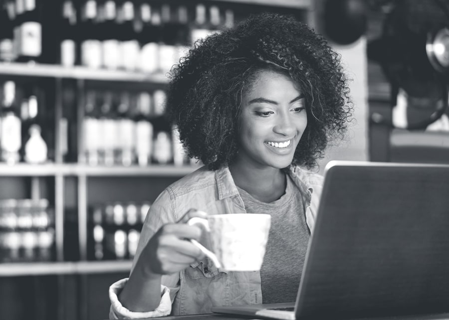 Woman smiling and holding a coffee cup while glancing at laptop