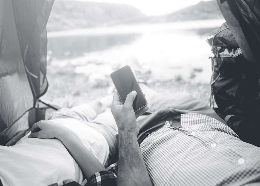 Two people laying on the ground in an open tent looking at water and cell phone
