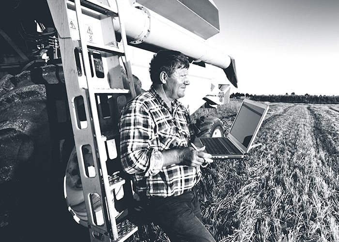 Man holding his laptop while standing beside farm equipment in field