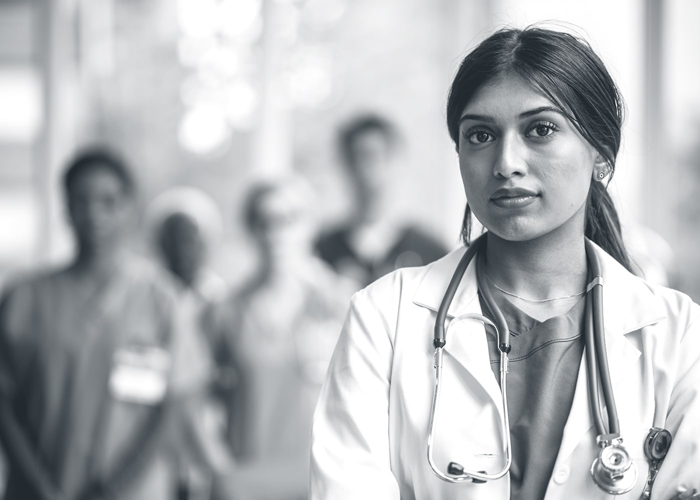 Female doctor looking straight ahead with medical staff blurred in the background