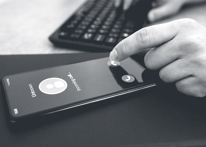 Hand pressing decline button on iPhone call with computer keyboard in background