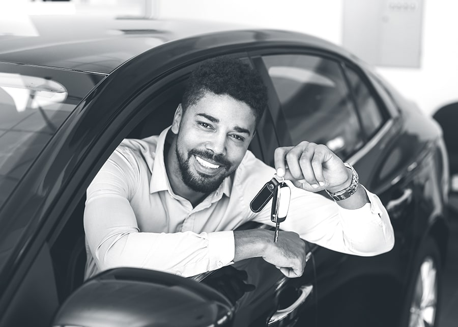 Smiling man in drivers seat holding car keys outside of car window while parked