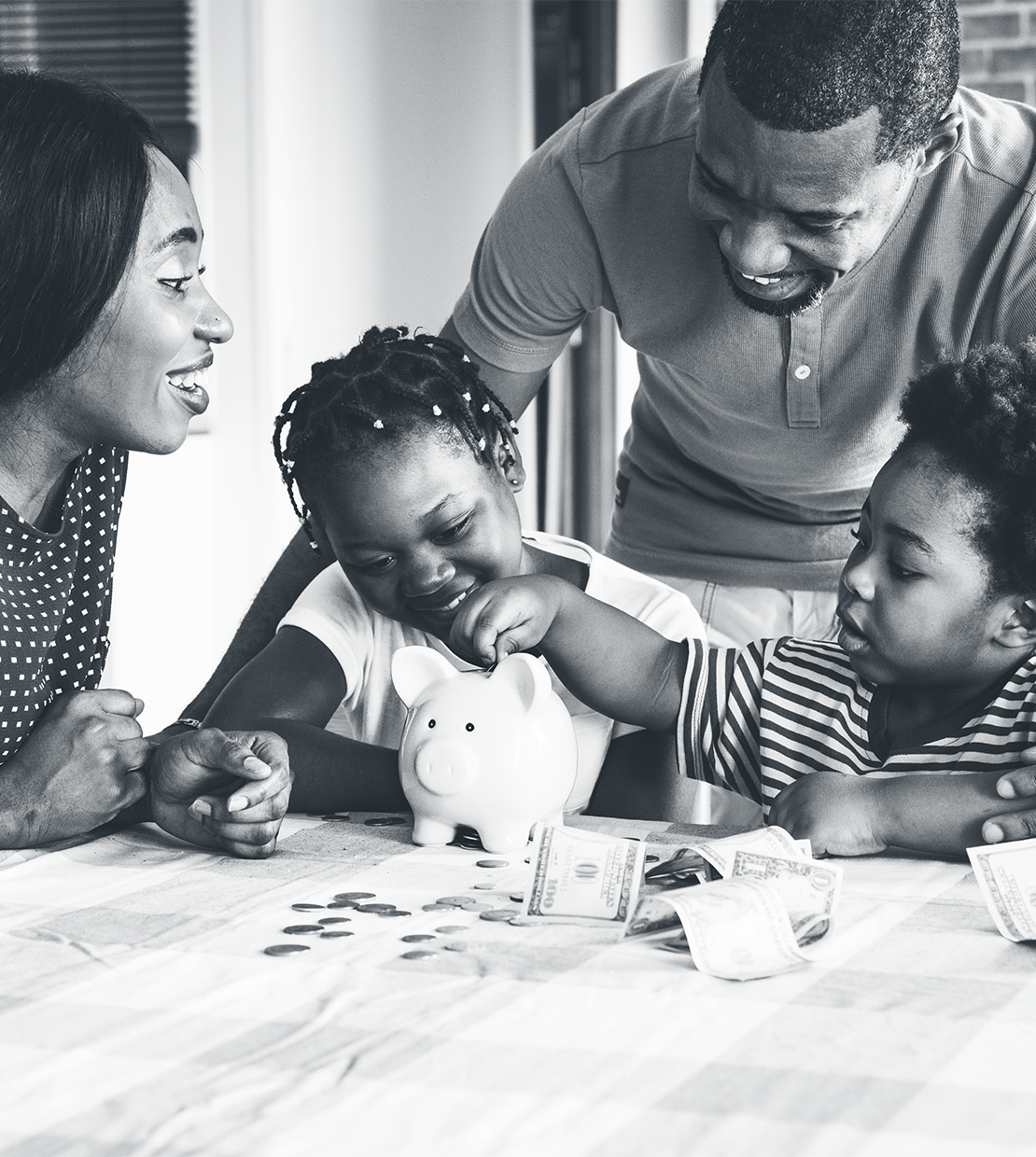 African American family of four smiling and looking down at a piggy bank with cash on the table