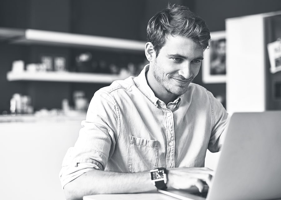 Man sitting in kitchen looking at his laptop