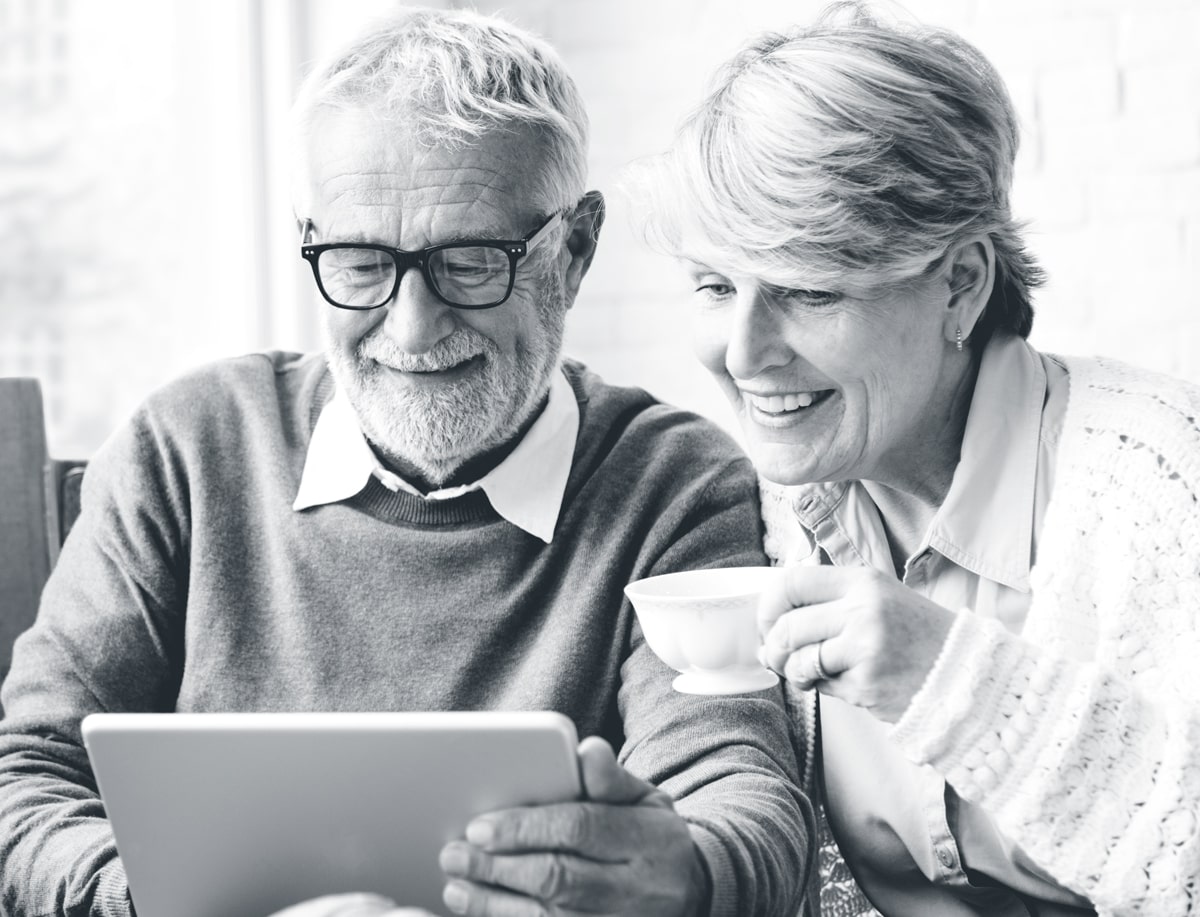 Smiling man holding an iPad sitting next to a smiling woman holding a tea cup